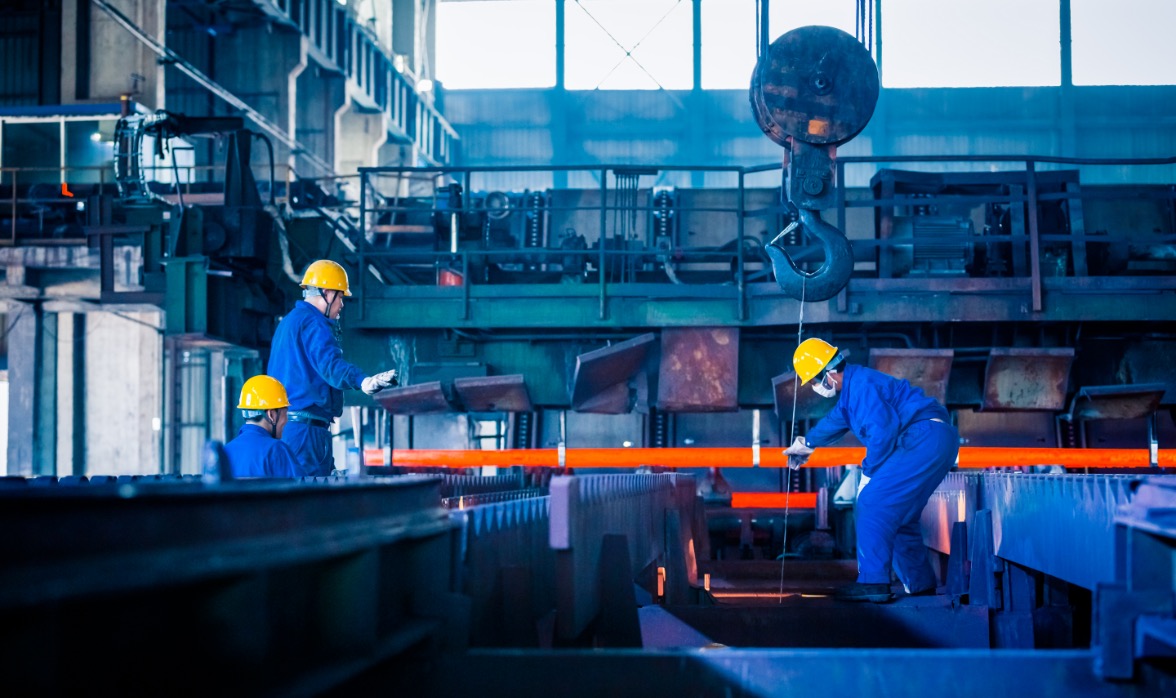 Arbeiter in Schutzkleidung bei der Stahlbearbeitung mit Kranhaken