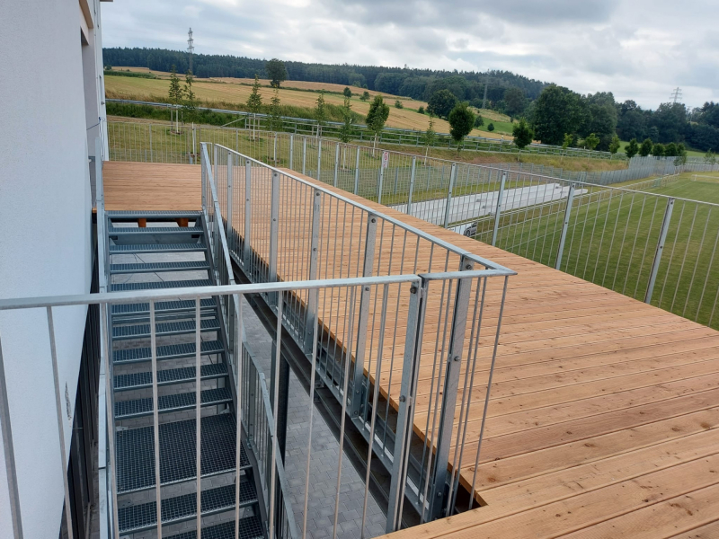 Holzterrasse mit Stahlgeländer und Treppe in ländlicher Umgebung