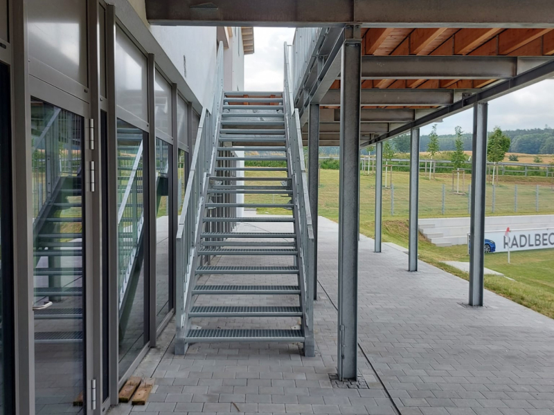 Stahltreppe mit Gitterroststufen unter Holzbalkendecke