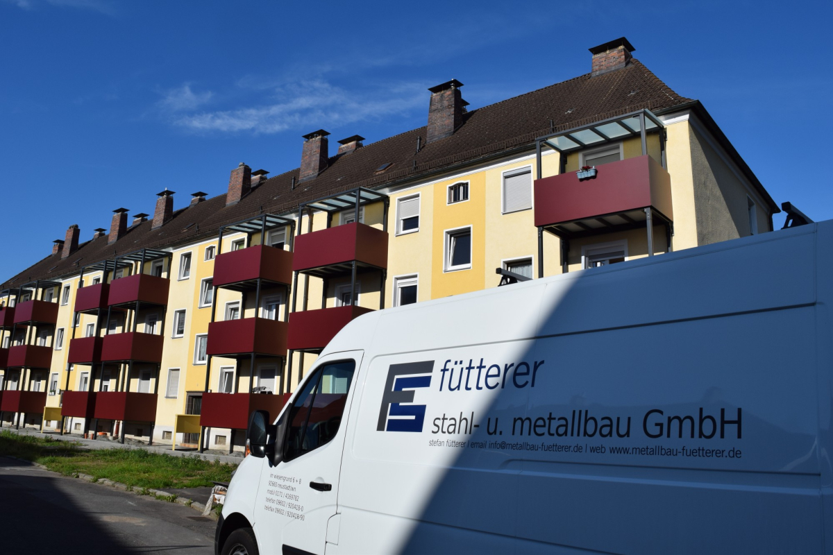 Firmenfahrzeug vor Wohnhaus mit neu montierten Stahlbalkonen