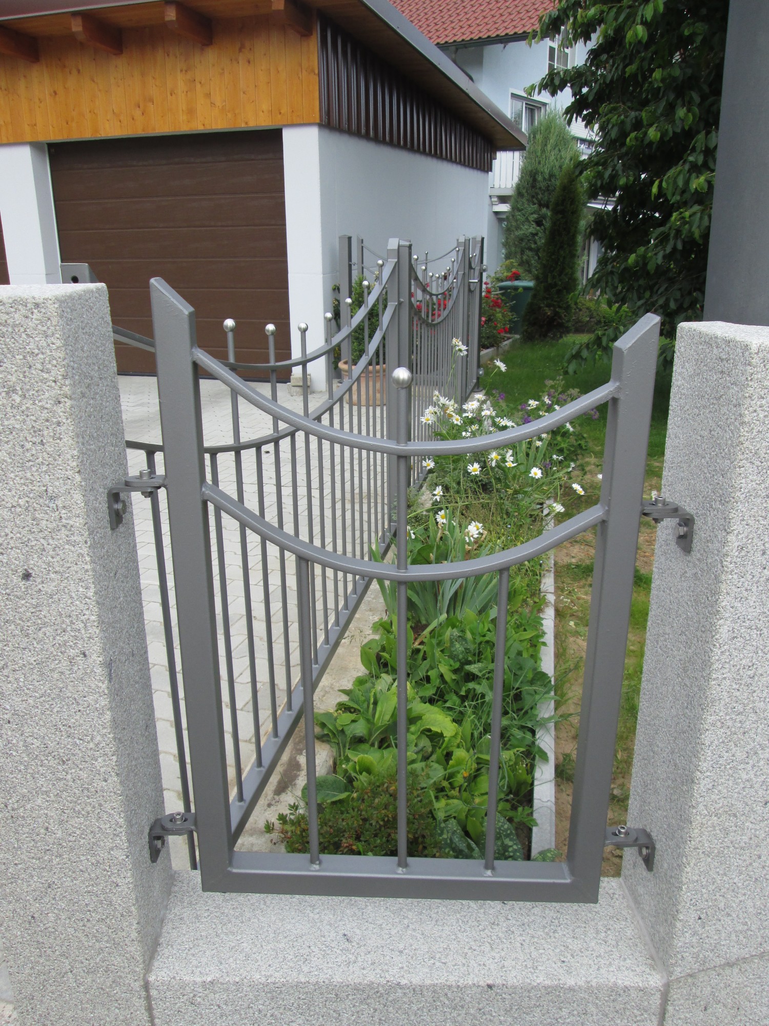 Graues Metalltor mit geschwungenen Zierstäben zwischen Granitsäulen